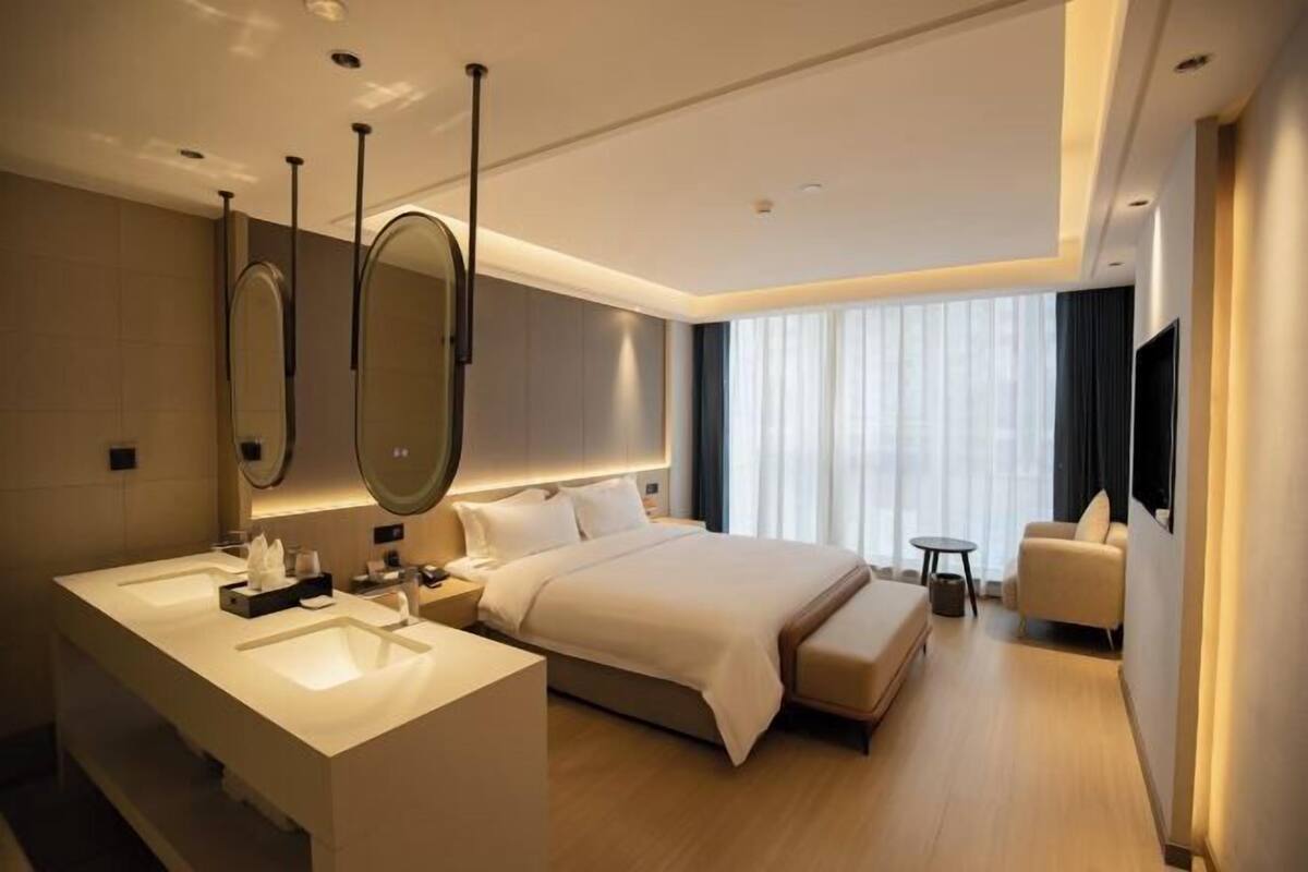 A modern hotel room with a large bed, a separate bathroom with a vanity, a small round table, and a chair.