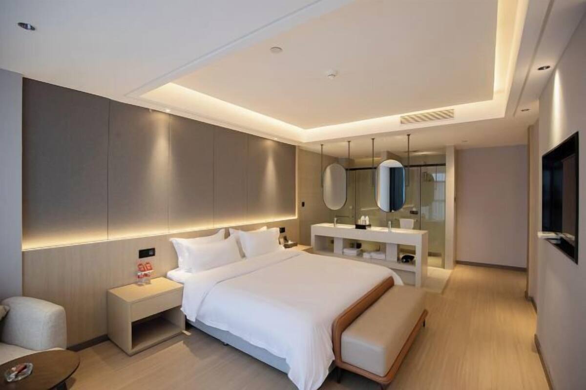 A modern hotel room with a large bed, bedside tables, a vanity with a mirror, and a flat-screen TV.
