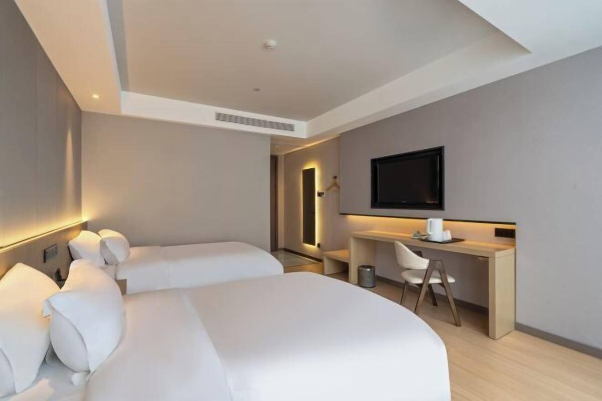 A hotel room with two beds, a desk, a chair, a television, and a small table.