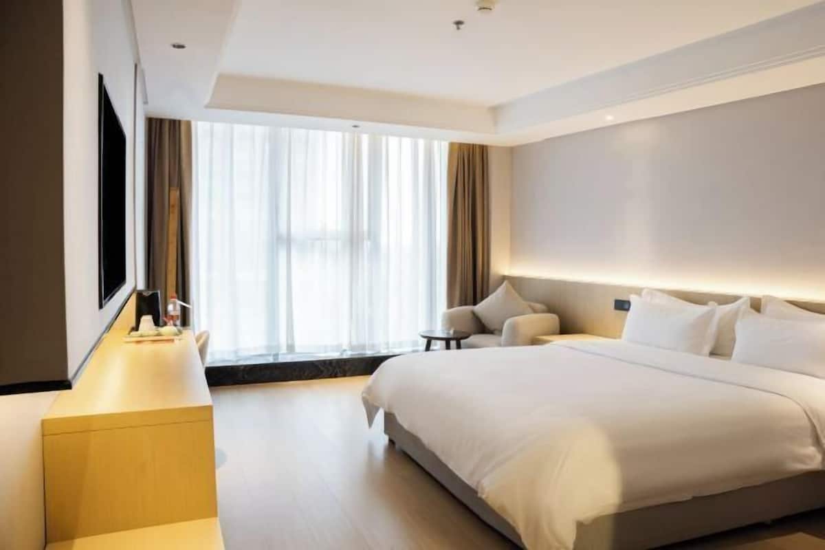 A modern hotel room with a large bed, a desk, and a TV.