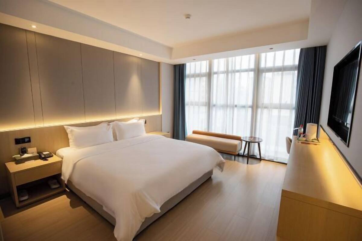A modern hotel room with a large bed, bedside table, and a seating area with a small table and chair.