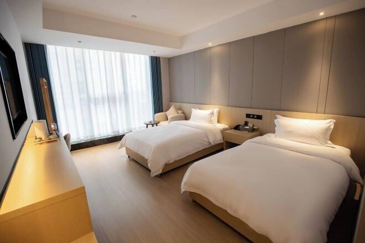 A hotel room with two beds, a desk, and a large window with curtains.