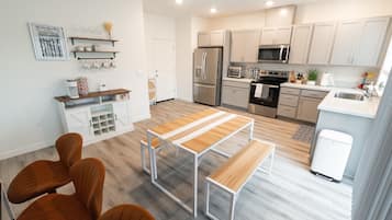 Una cocina moderna con armarios blancos, electrodomésticos de acero inoxidable y una mesa de madera con bancos.
