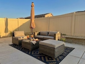 An outdoor seating area with wicker furniture, a table with drinks, and a patterned rug.