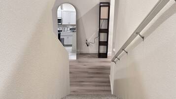 Una escalera con un rellano alfombrado que conduce a una zona de cocina con armarios blancos y piso de madera.