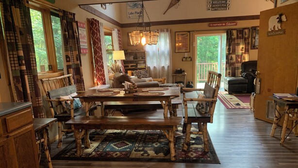 A cozy dining area with a wooden table and chairs, a patterned rug, and a view of the outdoors.