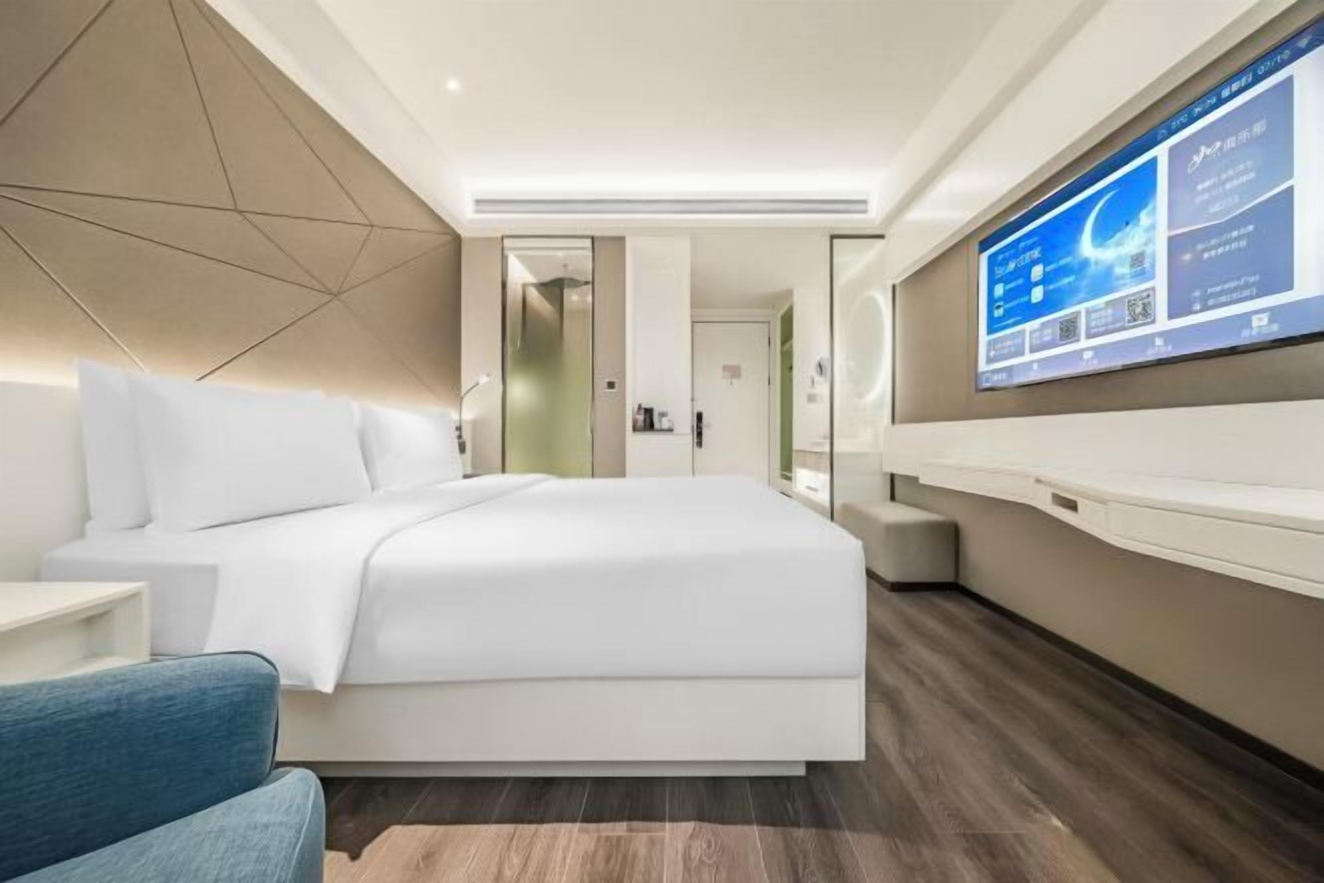A modern hotel room with a large bed, a TV mounted on the wall, and a desk with a chair.