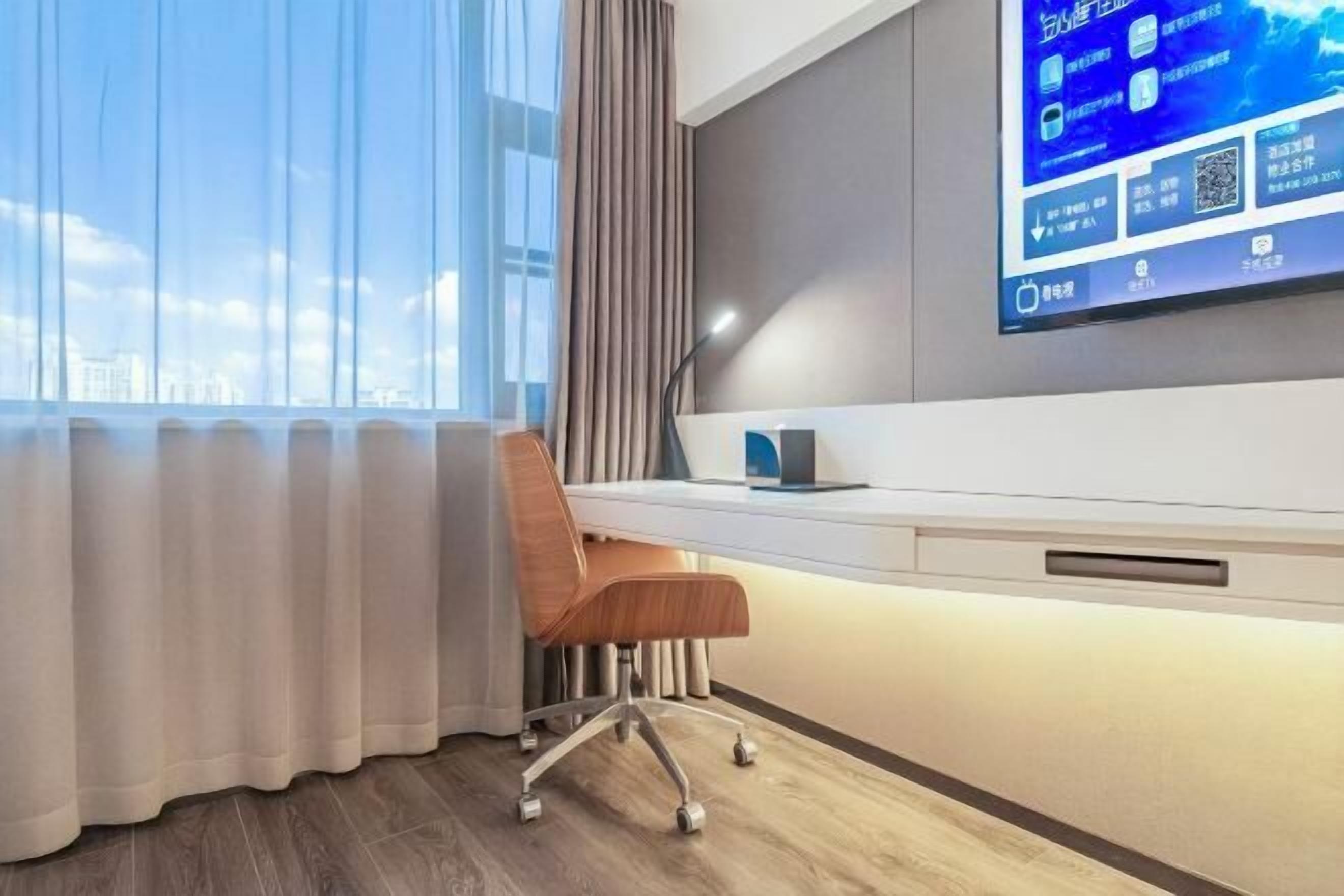 Een moderne hotelkamer met een groot raam, een bureau met stoel, en een tv met een digitaal scherm.