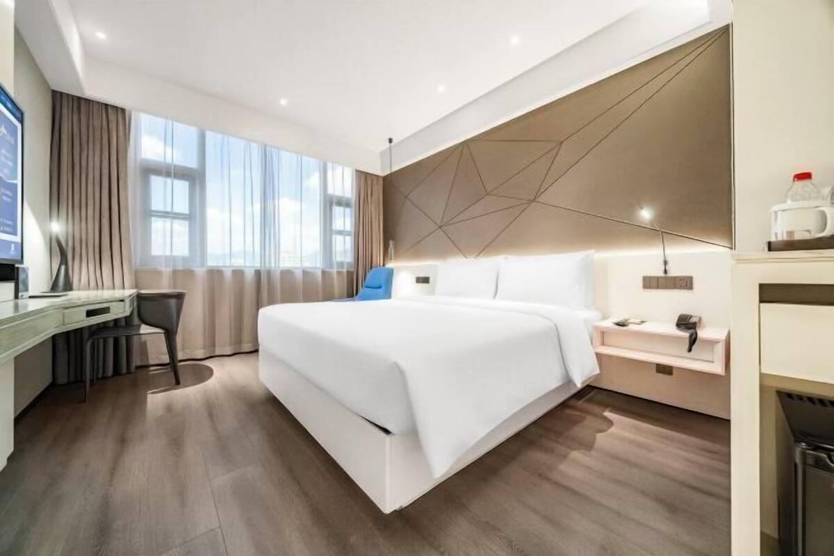 A modern hotel room with a large bed, a desk, and a view of the sky.