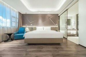 Une chambre d’hôtel moderne dotée d’un grand lit, d’un coin salon, d’une paroi en verre et offrant une vue sur le ciel.