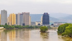 A river with a traditional pagoda-style building on the right and modern high-rise buildings in the background.