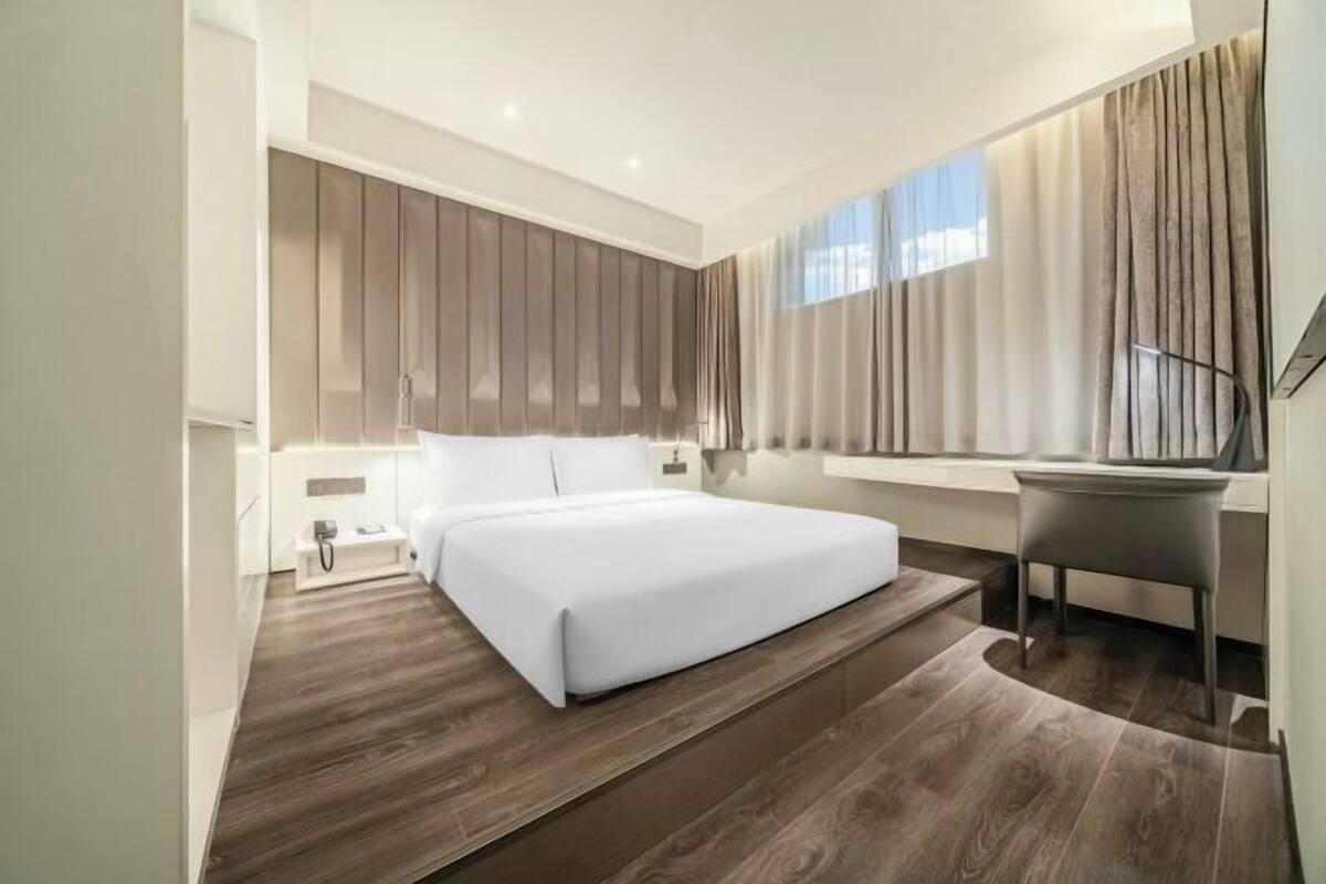 A modern hotel room with a large bed, a desk, and a window with curtains.