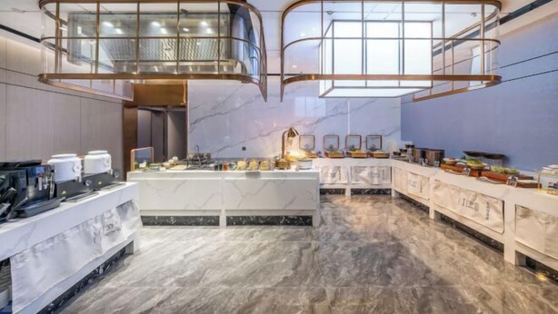 A modern hotel kitchen with marble countertops, a central island, and a mezzanine with glass railings.