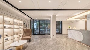 Un área de recepción moderna con suelo de mármol, una mesa de recepción y una zona de estar con una silla y una mesa.