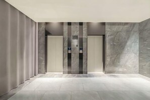 Área de elevador moderna com paredes de mármore e chão em mosaico.