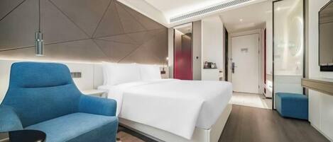 A modern hotel room with a large bed, a blue armchair, a bedside table, and a mirror.