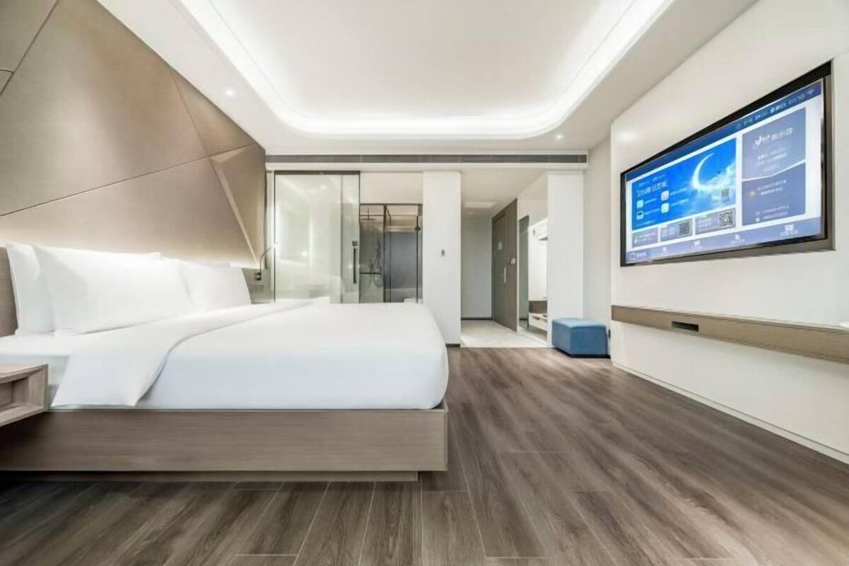 A modern hotel room with a large bed, a flat-screen TV, and a wooden floor.