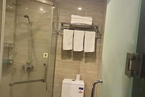 A shower area with a glass door, a towel rack with folded towels, and a toilet paper holder.