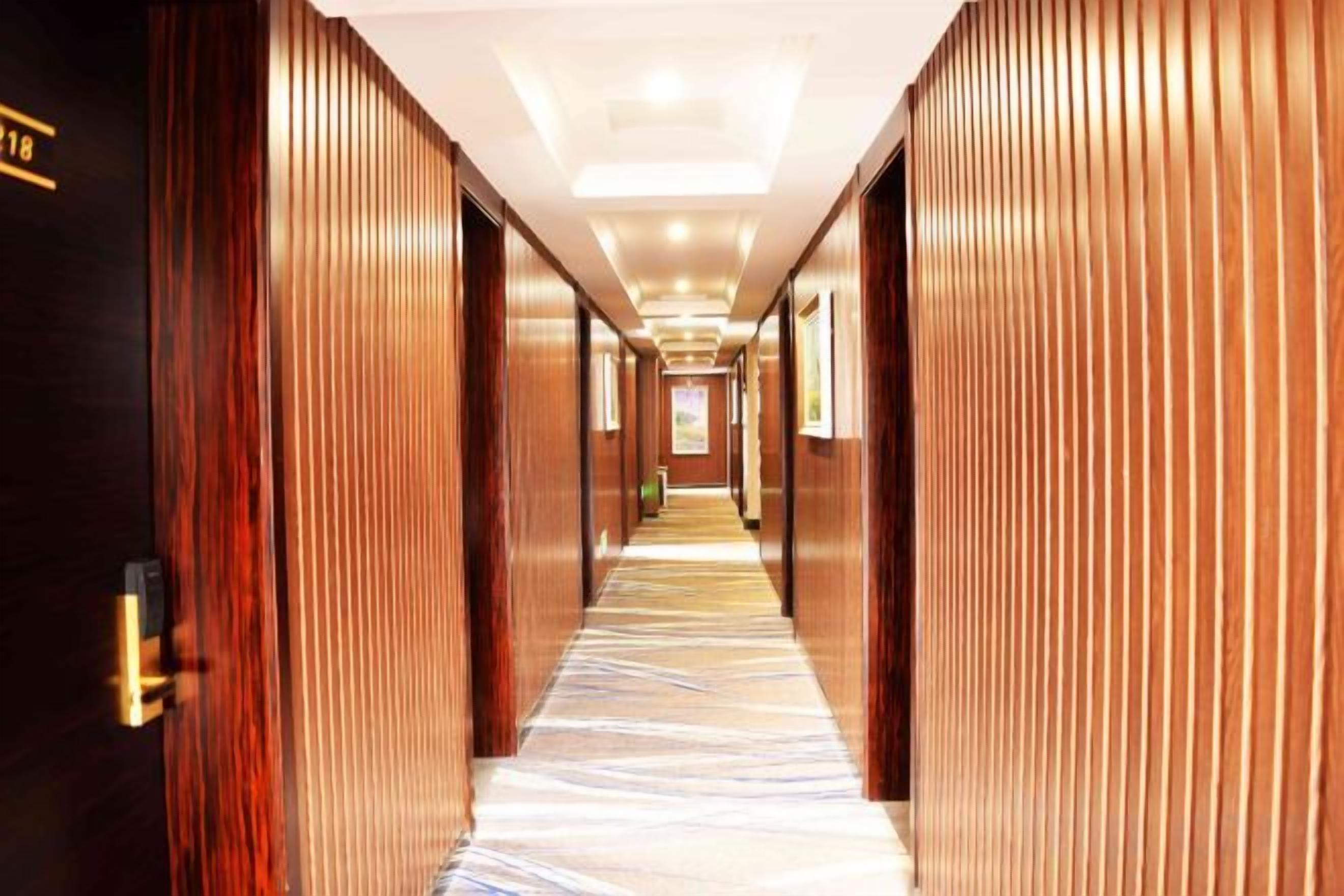 A hotel corridor with wooden paneling, a carpeted floor, and a ceiling with recessed lighting.