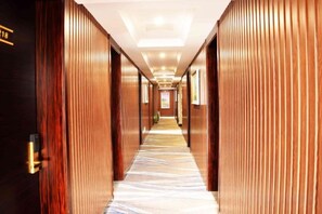 Pasillo de hotel con paneles de madera, piso alfombrado e iluminación empotrada en el techo.
