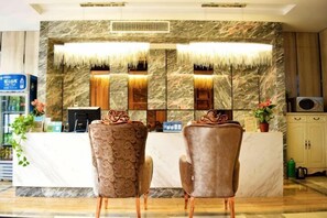 A reception area with a marble wall, two patterned chairs, a reception desk, and a plant. - Kaiwang Hotel (Nanjing Mingguo Subway Station Military General Hospital) (Nanjing)