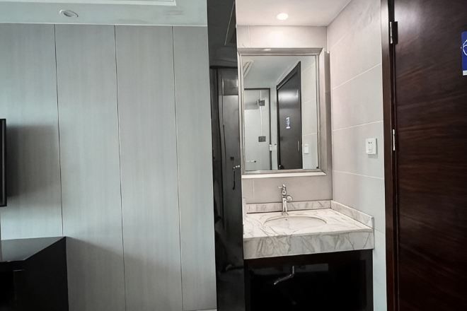 A modern bathroom with a large mirror, a sink, and a dark wooden door.