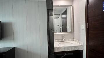 A modern bathroom with a large mirror, a sink, and a dark wooden door.