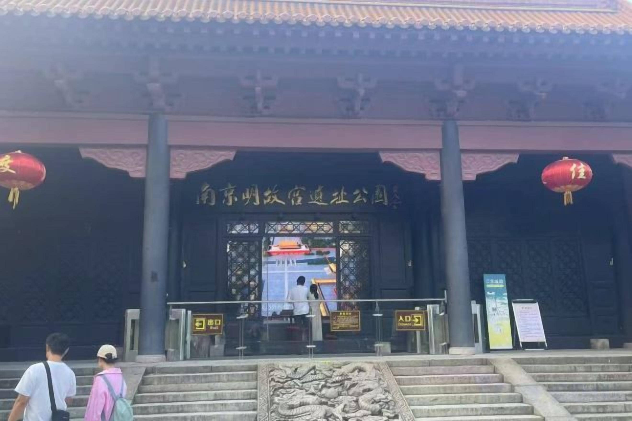 A traditional building entrance with steps leading up to a gate, a signboard, and a red lantern.