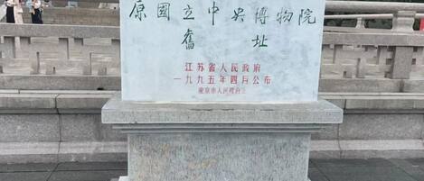 A stone monument with inscriptions in Chinese characters, located in an outdoor setting with steps and a railing in the background.