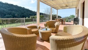 Une terrasse extérieure couverte, aménagée avec des meubles en osier, une table avec des verres et un barbecue.