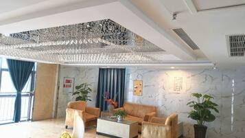 Eine Hotelhalle mit hoher Decke, Marmorwänden, einem Chandelier, zwei Sofas, einem Couchtisch und Kübelpflanzen.