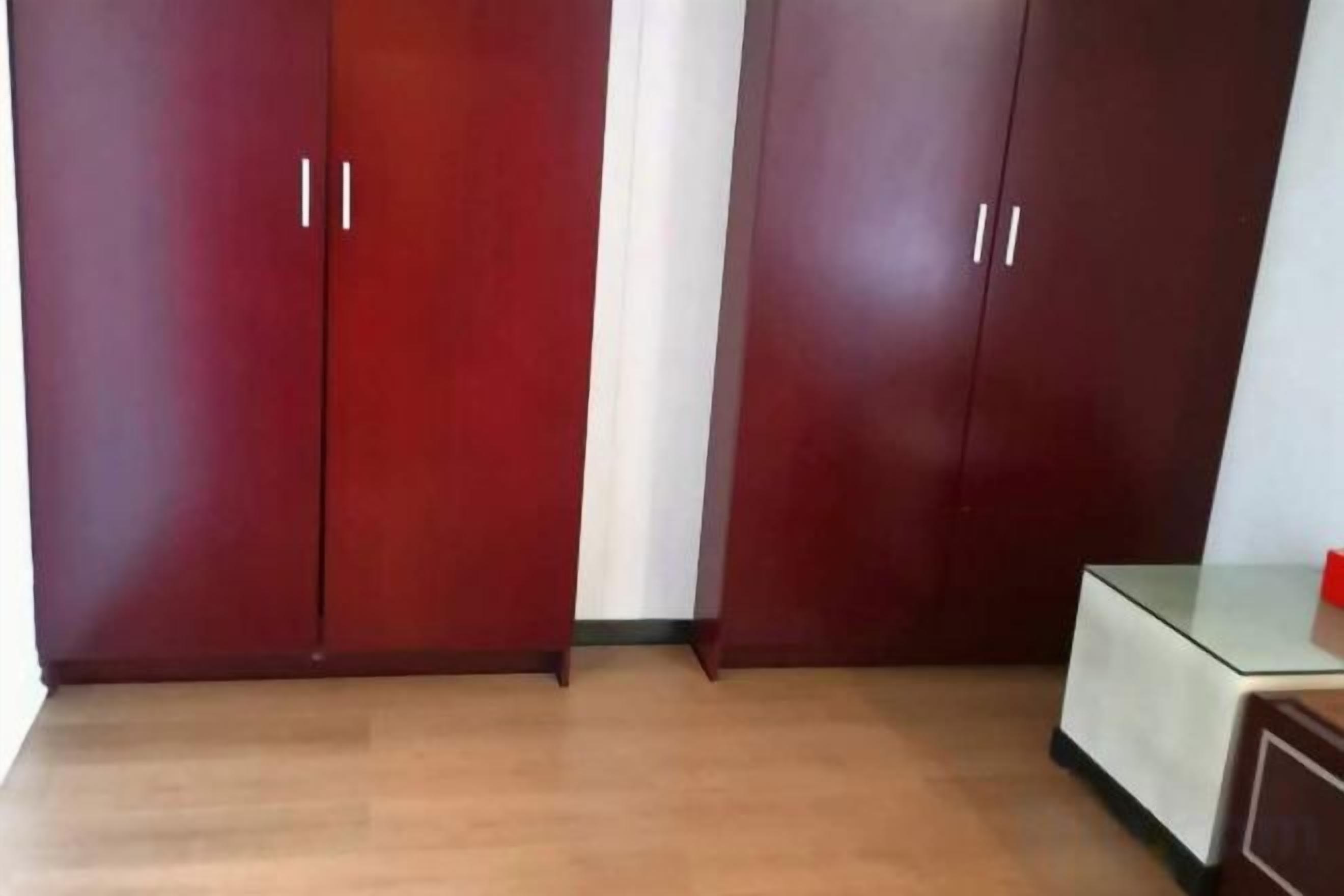 A room with two wooden wardrobes, a glass table, and a wooden cabinet.