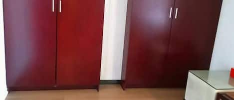 A room with two wooden wardrobes, a glass table, and a wooden cabinet.