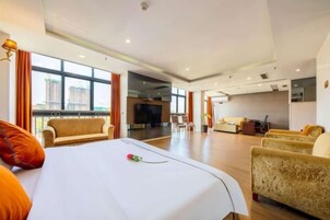 Quarto de hotel com cama grande, sofá, televisão e vista para a cidade.