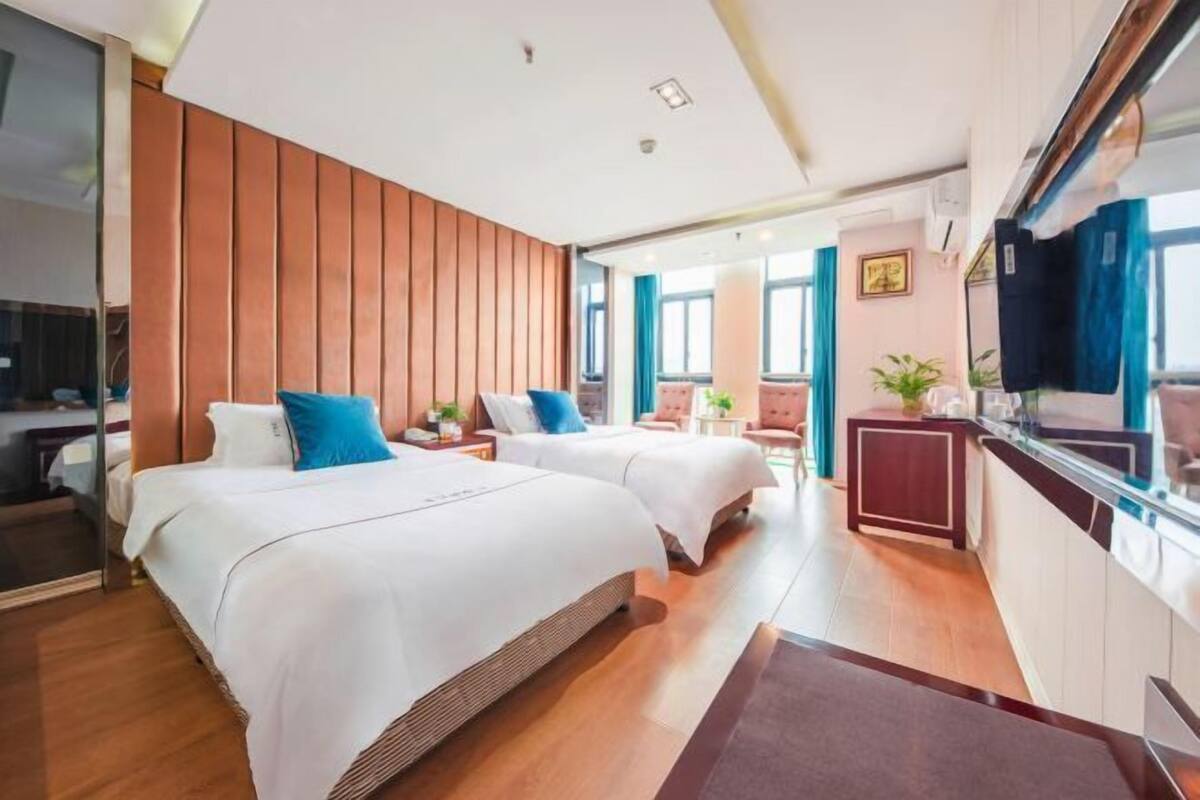 Hotellihuone, jossa on kaksi sänkyä, puusta tehty koristeellinen seinä, pieni keittokomero ja näkymä kaupunkiin.