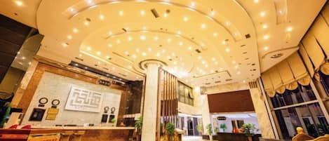 Een hotellobby met een receptiebalie, een grote pilaar en een gebogen plafond met verlichting.