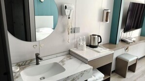 Une salle de bain moderne équipée d’un lavabo, d’un miroir, d’un sèche-cheveux et d’un téléviseur fixé au mur.