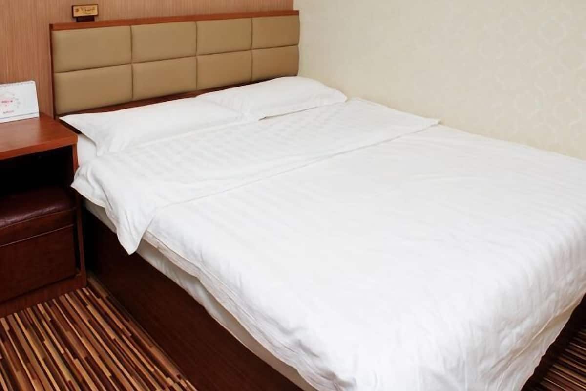 A hotel room with a bed, a nightstand, and a wooden floor.