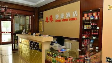 A reception desk with a glass partition, a signboard, and a display of bottled beverages.