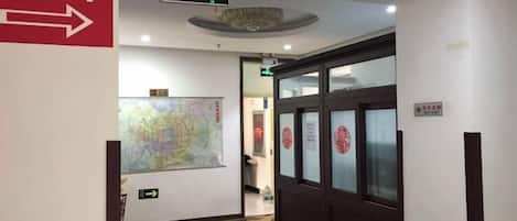 A hotel corridor with an exit sign, a map on the wall, and a door with frosted glass panels.