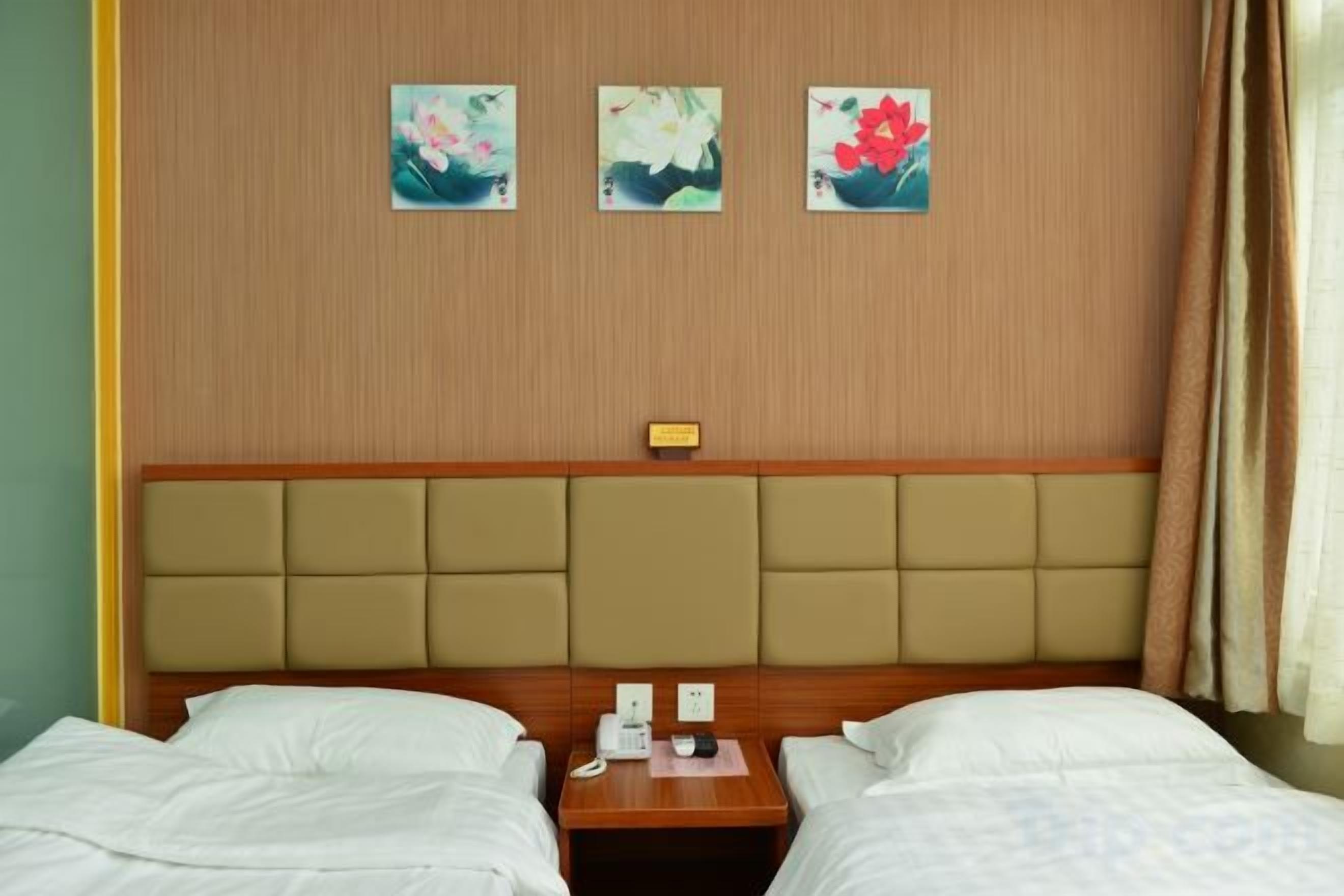 Habitació d'hotel amb dos llits, un capçal de llit de fusta i tres quadres florals a la paret.