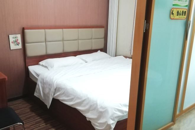 A hotel room with a bed, a wooden headboard, a bedside table, and a wall-mounted sign.