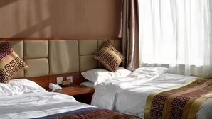 Habitación de hotel con dos camas, cabecero de madera, mesita de noche y ventana con cortinas.