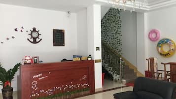 A reception desk with a clock and a framed picture on the wall, a staircase with a green wall, and a black sofa in the foreground.