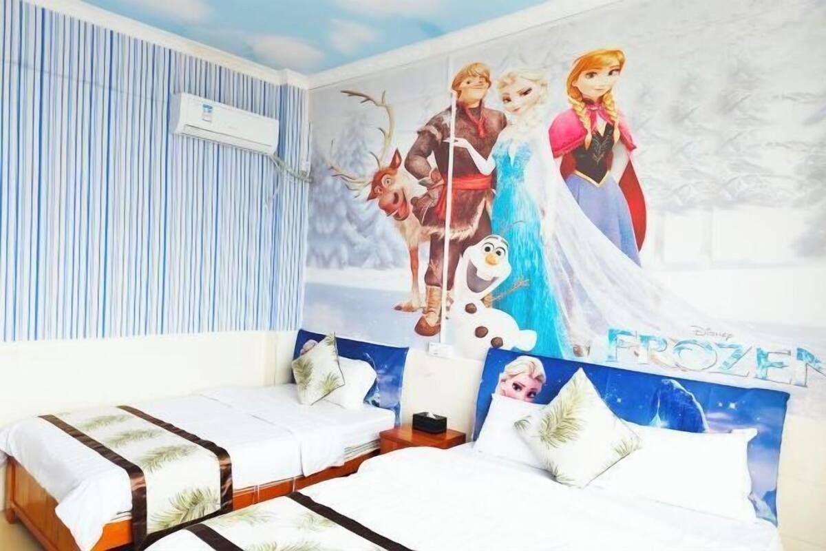 A hotel room with a bed, a wall-mounted air conditioner, and a poster of Frozen characters.
