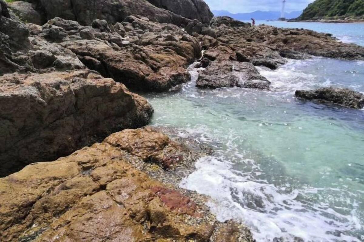 A rocky shoreline with clear water and a lighthouse in the distance.