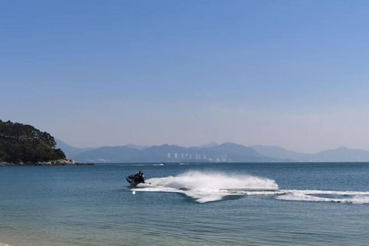 A person jet-skiing on a calm body of water with a distant mountain range and a bridge in the background.