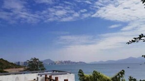Terraza en la azotea con barandilla de madera, con vistas a un cuerpo de agua y un horizonte urbano distante.