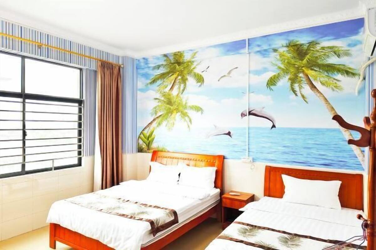 A hotel room with two beds, a large window with blinds, and a mural of palm trees and the sea.