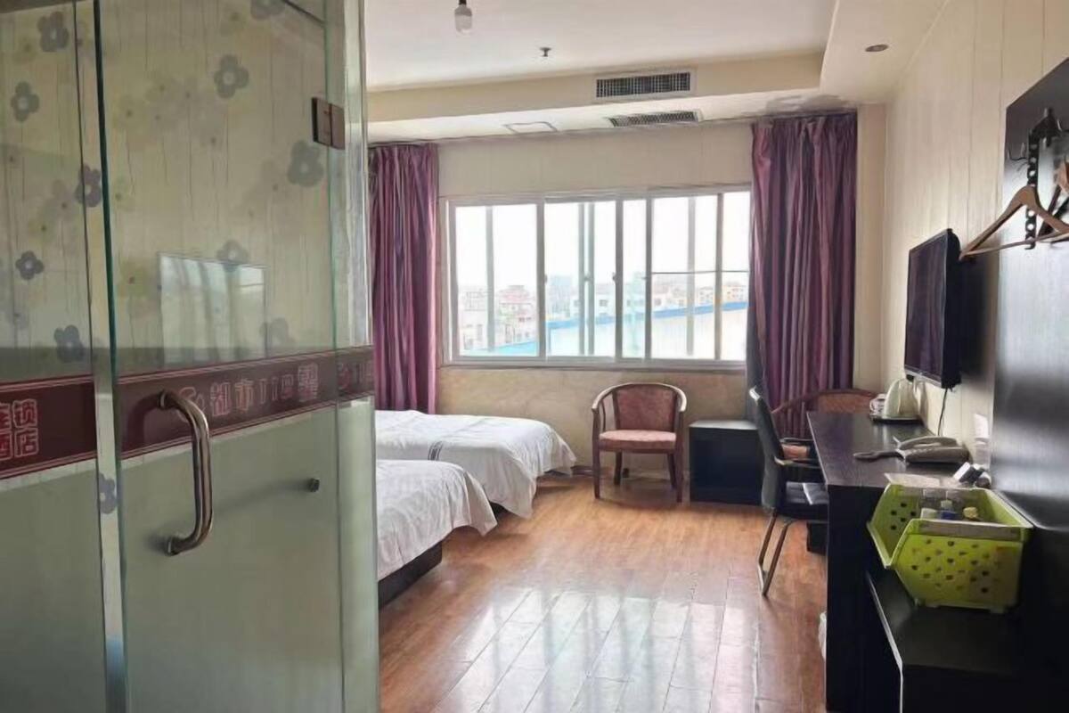 Habitación de hotel con dos camas, un escritorio, una silla, un televisor y una ventana con cortinas.